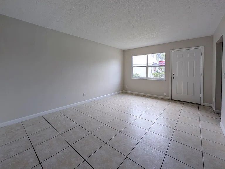 Empty room with tiled floor, white door and window, and light grey walls.