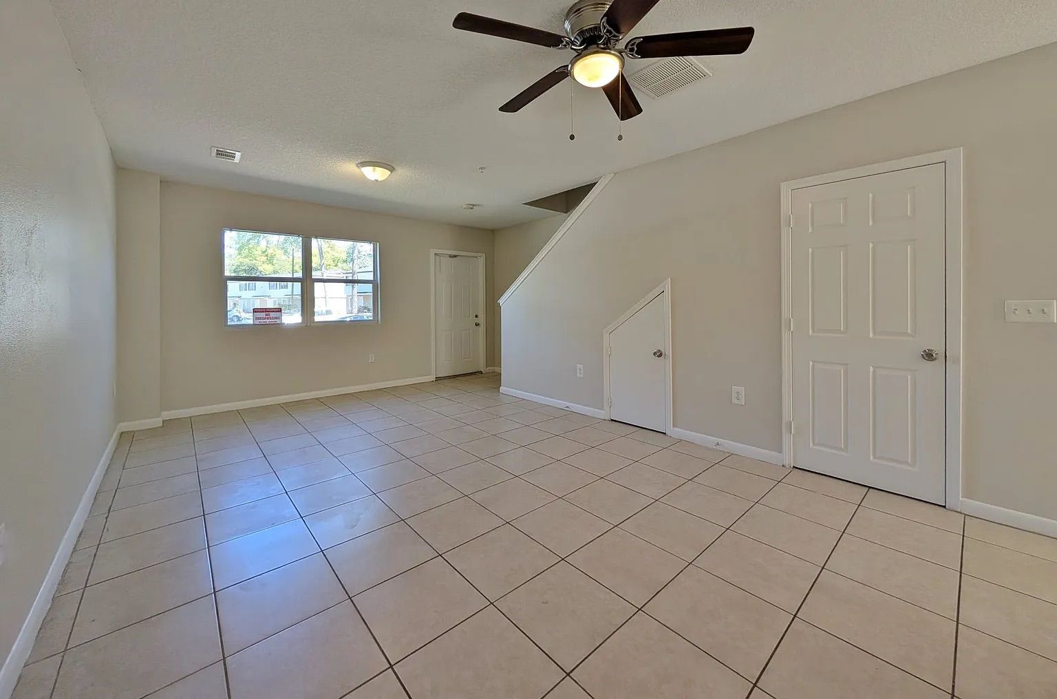 Empty living room with tiled floor, ceiling fan, stairs, and two white doors.