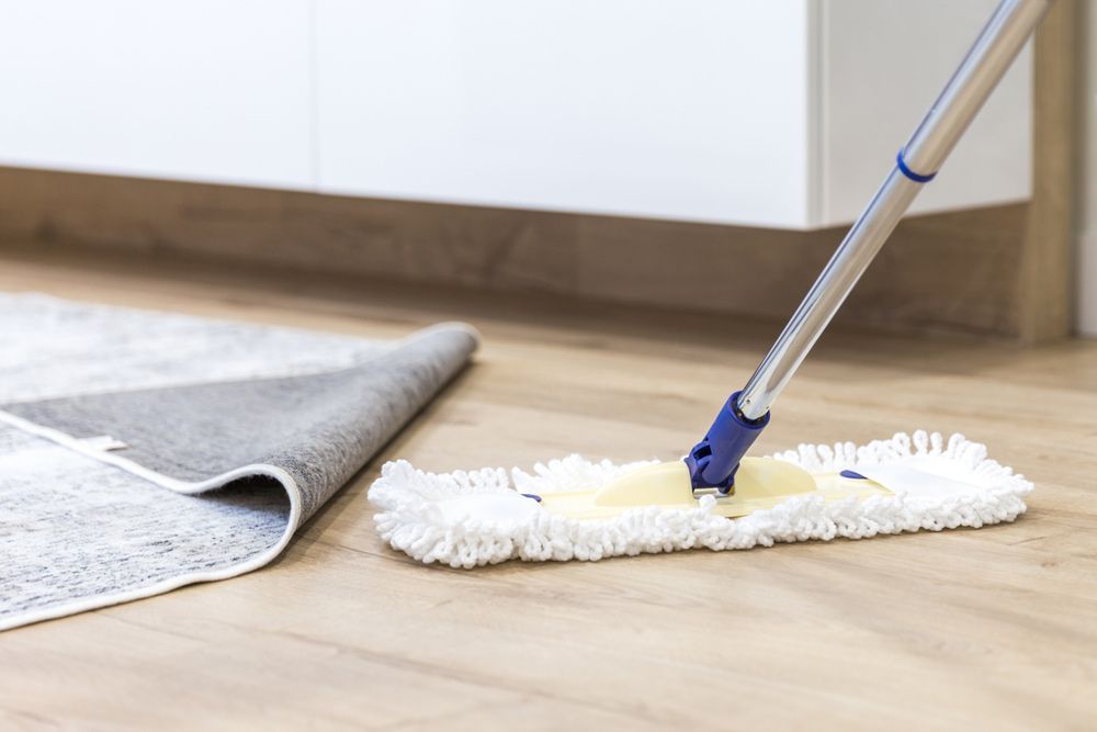 A Mop is Being Used to Clean a Wooden Floor Next to a Rug — Shane’s Car Detailing & Office Cleaning in Gunnedah, NSW