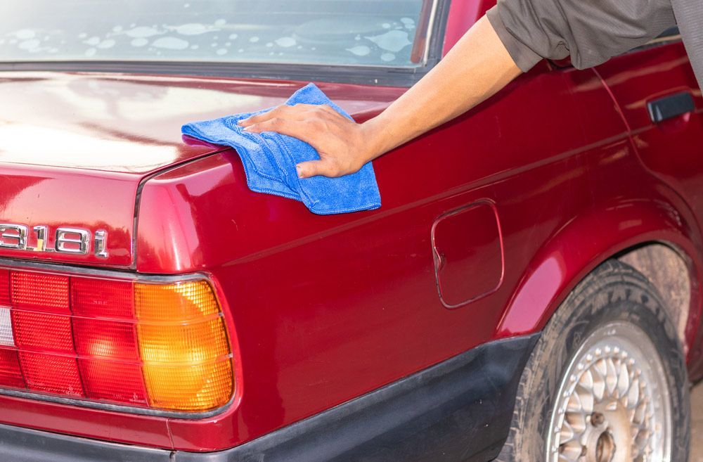 A Person is Cleaning a Red Car With a Blue Towel — Shane’s Car Detailing & Office Cleaning in Armidale, NSW