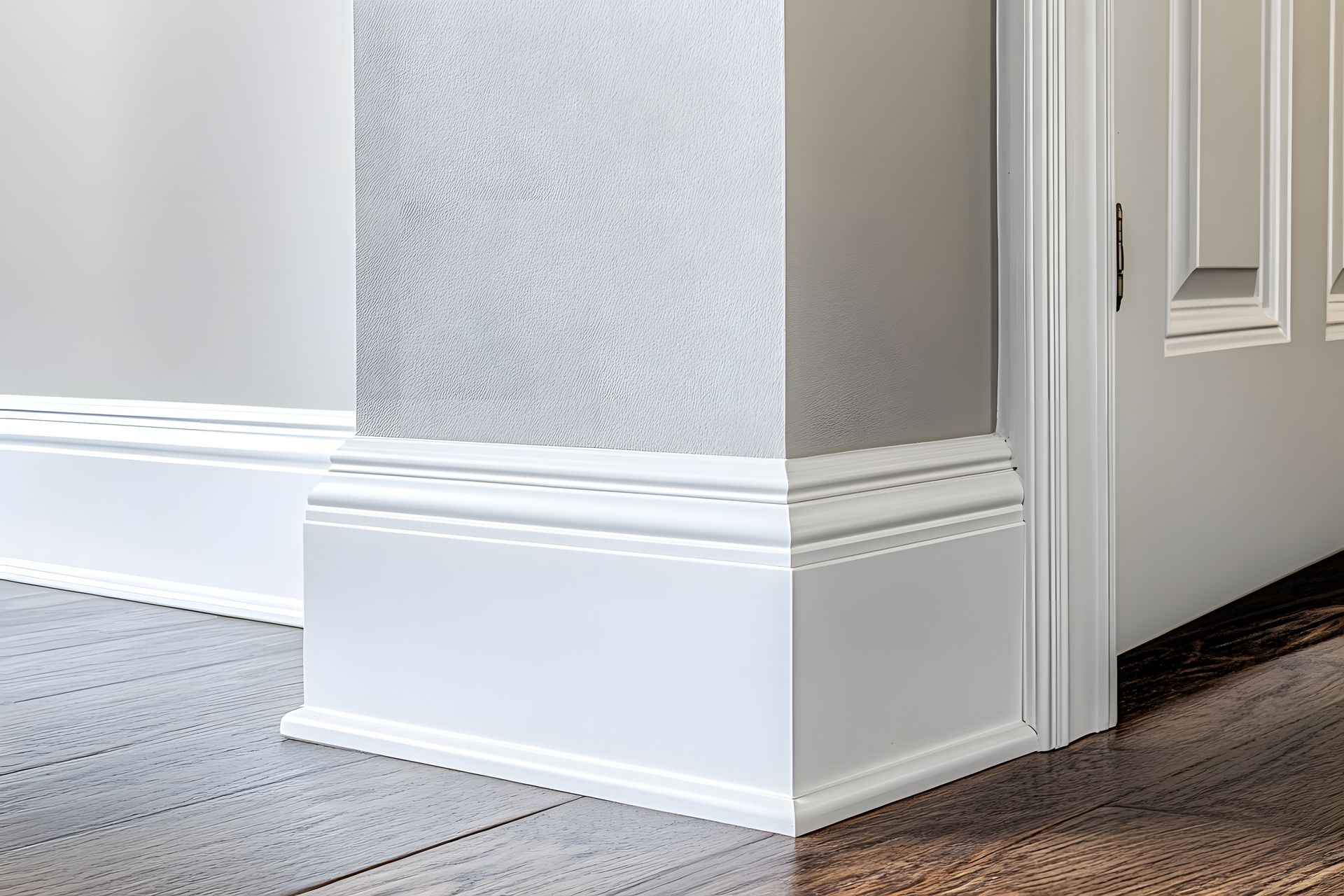 White baseboard molding at a corner of a room, with textured wall and wood floor.