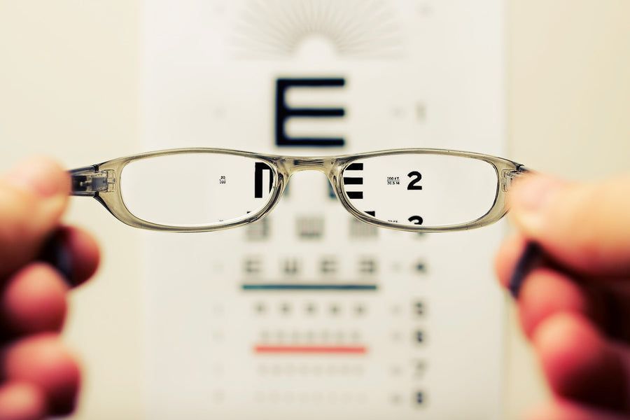 A person is holding a pair of glasses in front of an eye test chart.