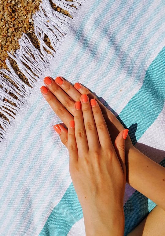 A woman with orange nails is sitting on a beach towel.