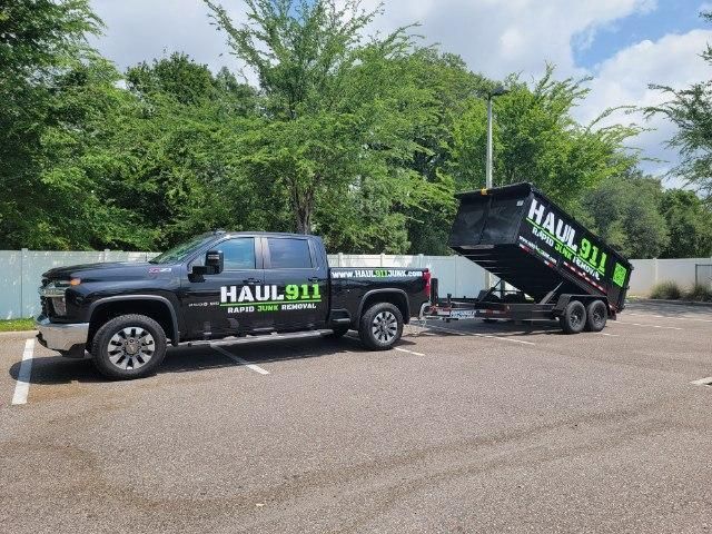 A black pickup truck parked in an outdoor lot, towing a raised, black dump trailer with neon green 