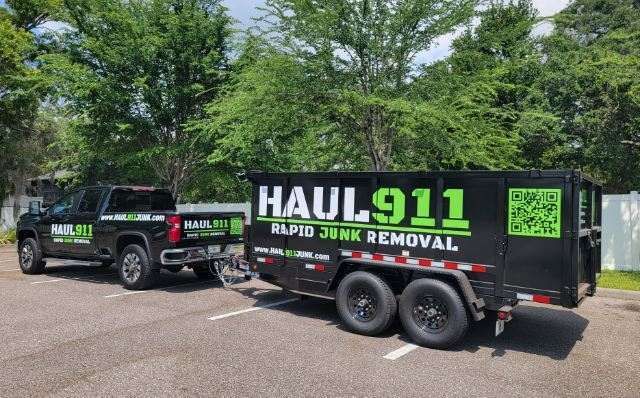 A black pickup truck towing a matching black dump trailer branded with 
