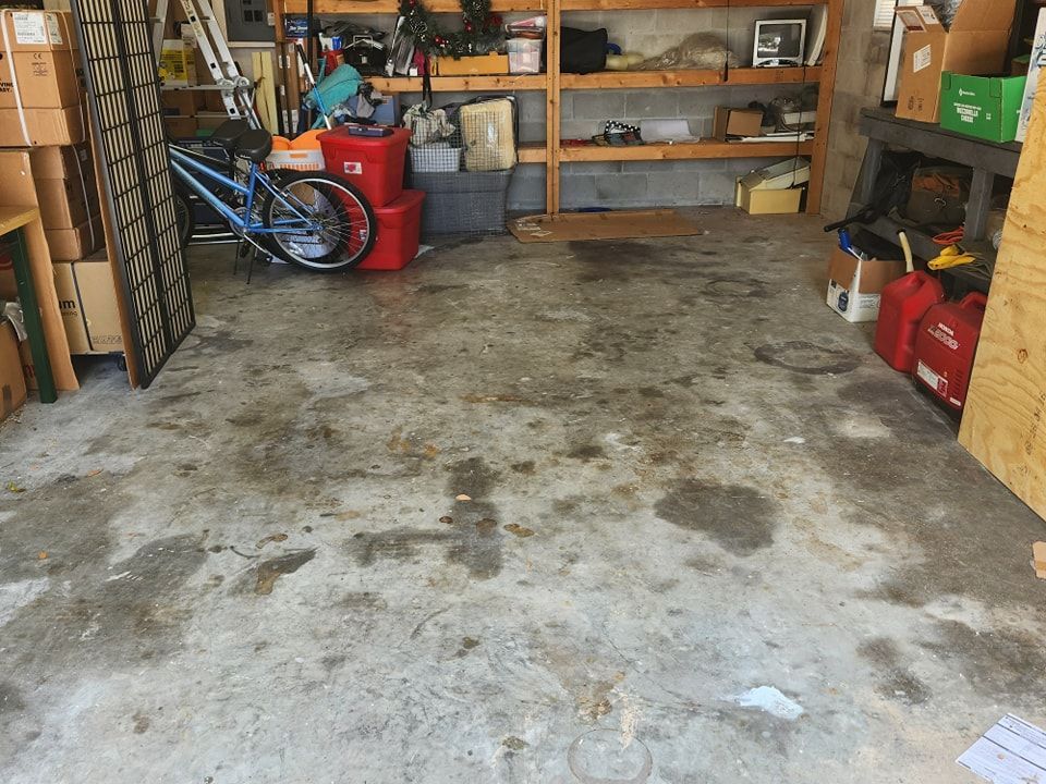 A cluttered garage interior with a stained concrete floor, shelving units, a blue bicycle, and various storage containers.