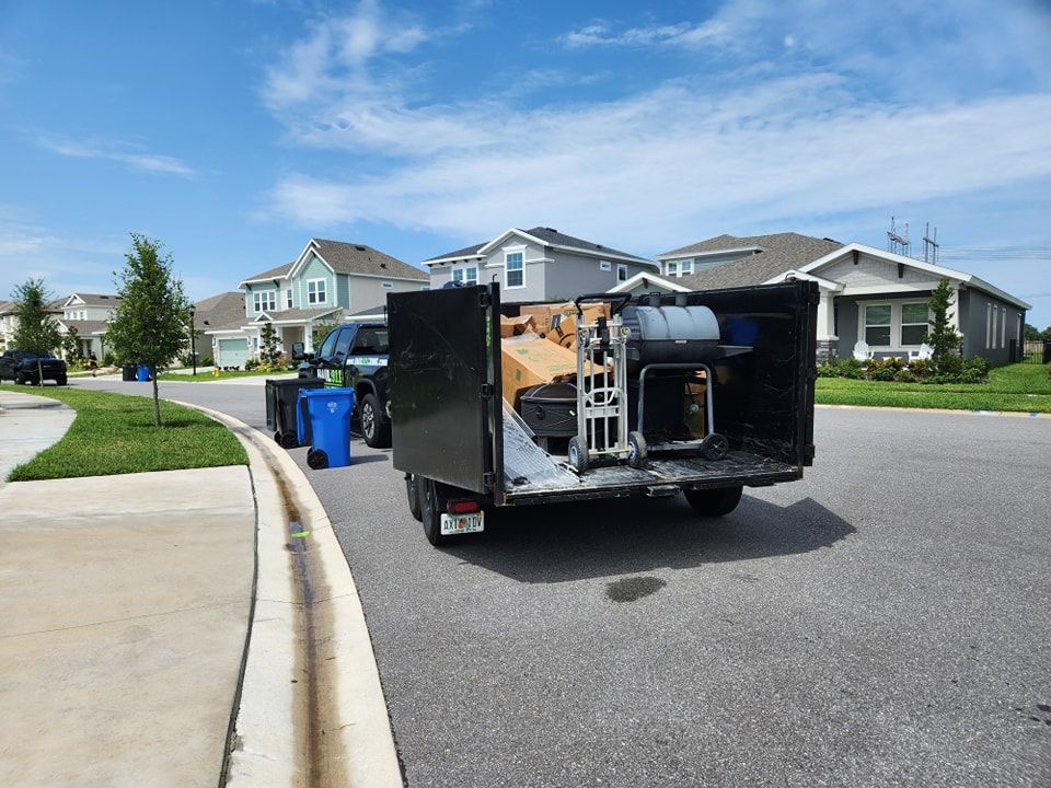 A black utility trailer loaded with equipment, hitched to a truck on a suburban residential street.