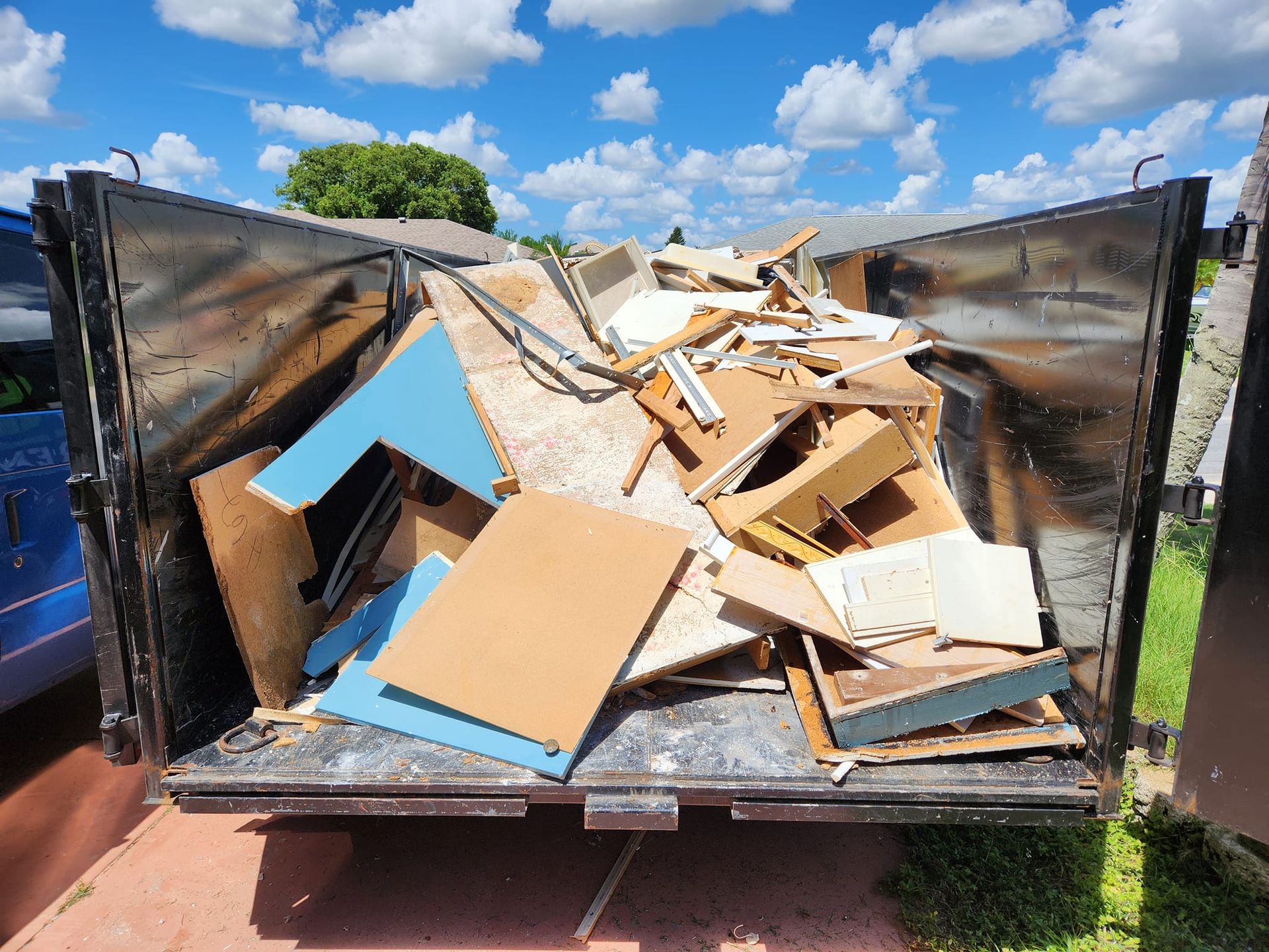 A large metal trailer filled with discarded wooden furniture, cabinets, and construction debris under a blue sky.
