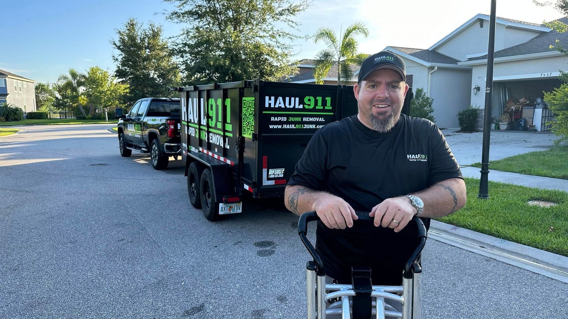 A man smiles in front of a black dump trailer labeled 