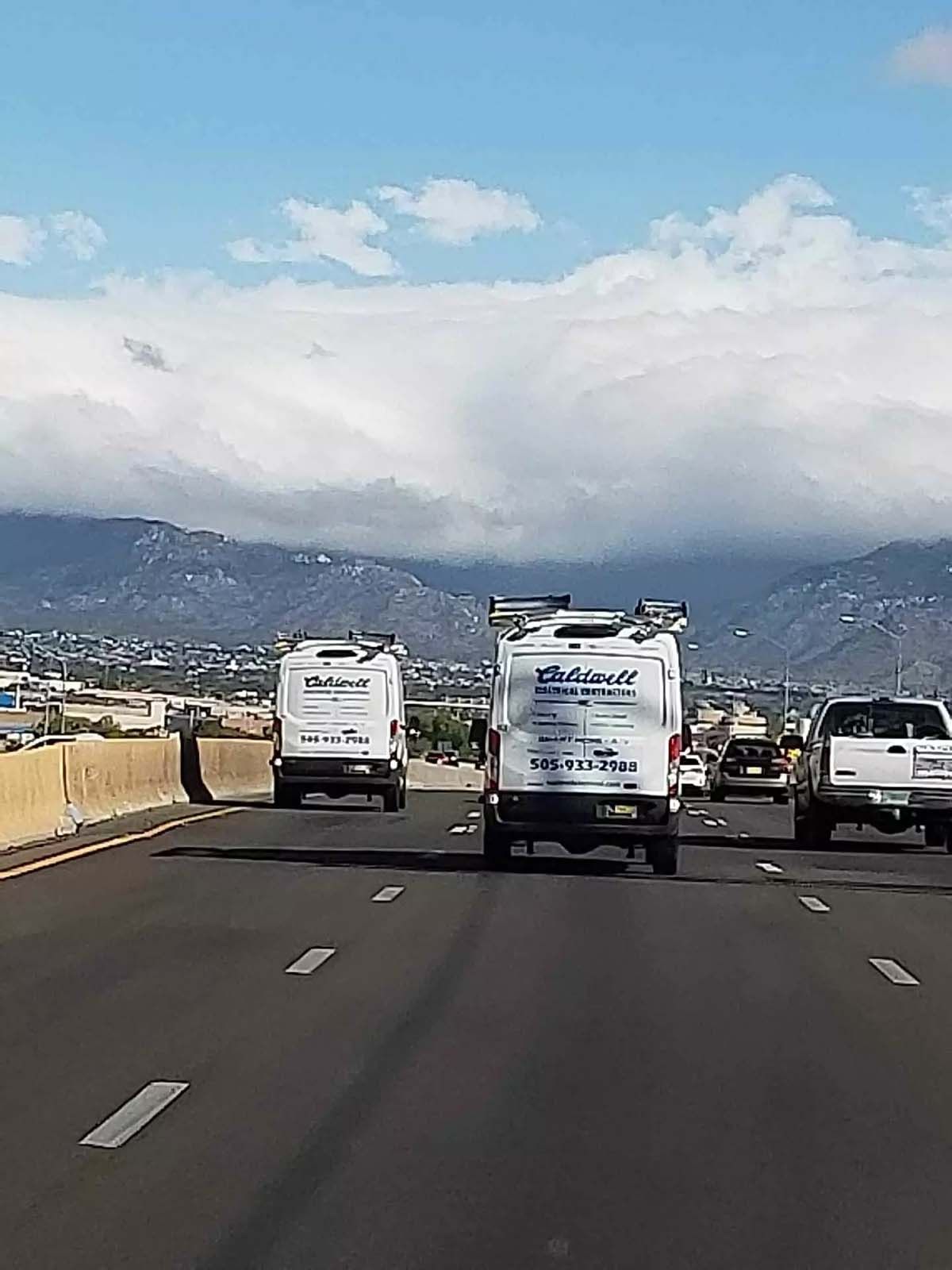 A row of vans are driving down a highway with mountains in the background.