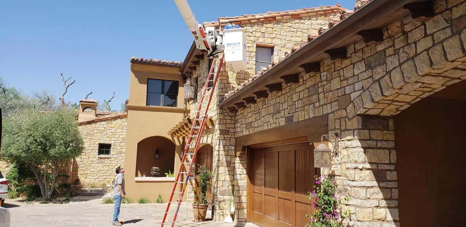 A man is standing on a ladder in front of a large stone building.