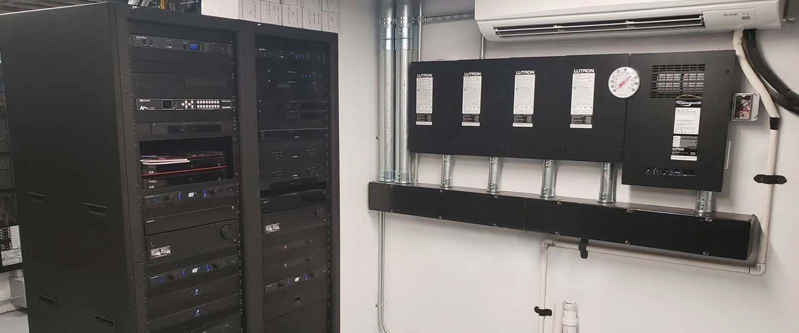 A room with a lot of servers and a fan on the wall.