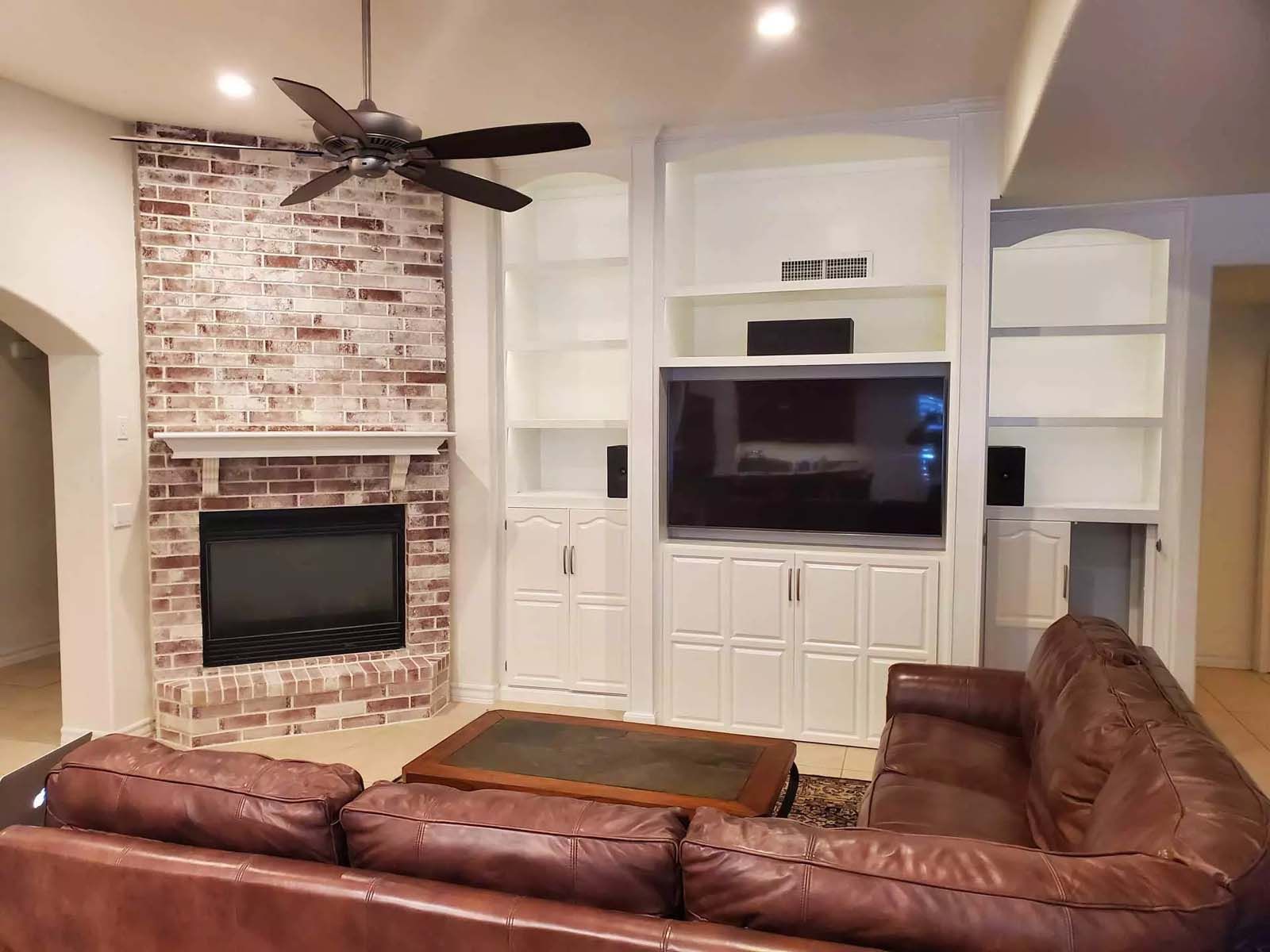 A living room with a couch , fireplace , television and ceiling fan.