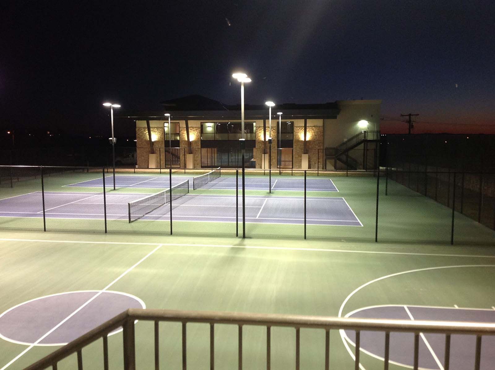 A tennis court and basketball court are lit up at night