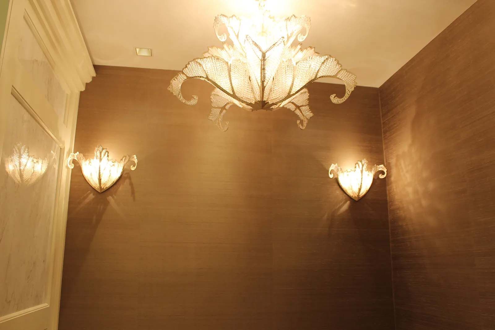 A bathroom with a chandelier hanging from the ceiling and two wall lights.