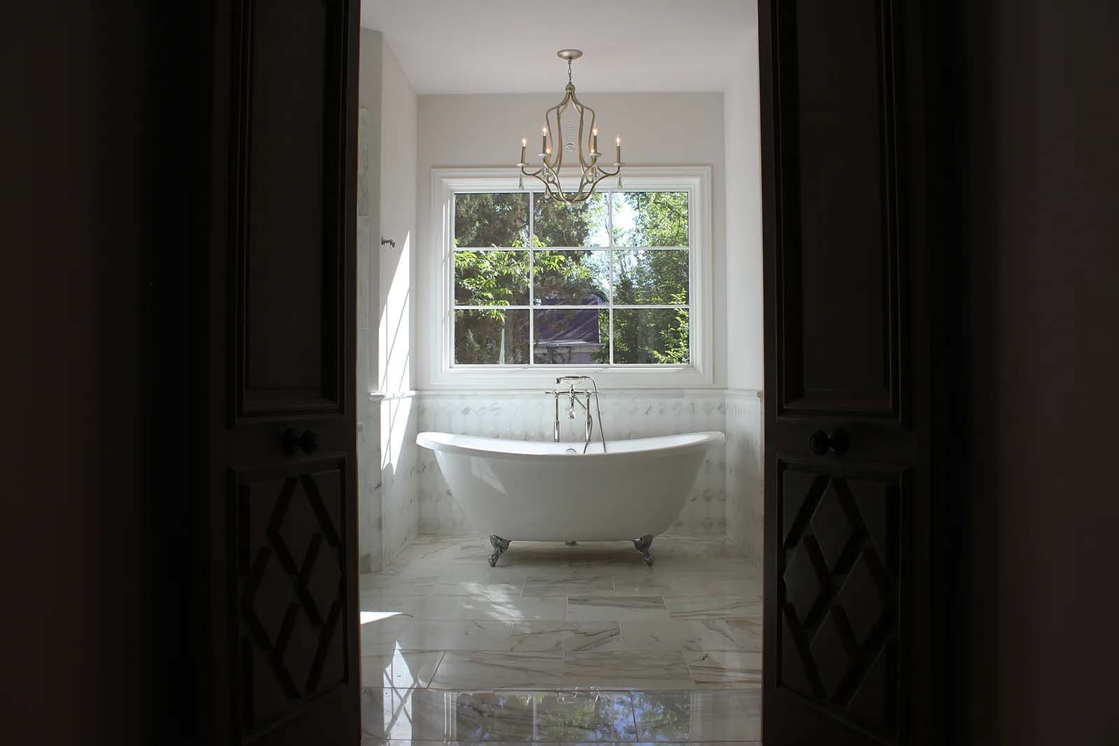 A bathroom with a tub and a window with a chandelier hanging from the ceiling.