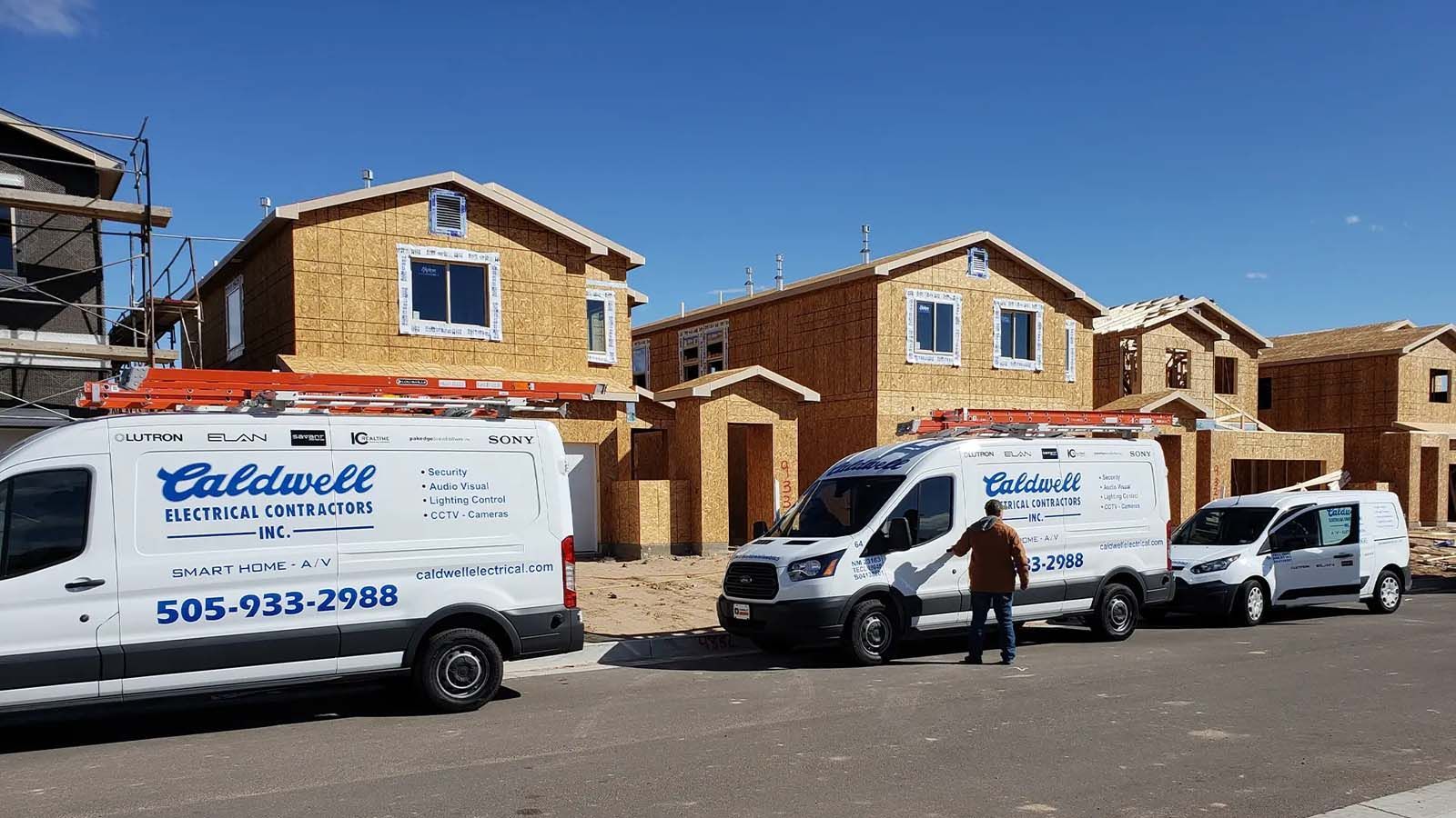 A row of white vans are parked in front of a building under construction.