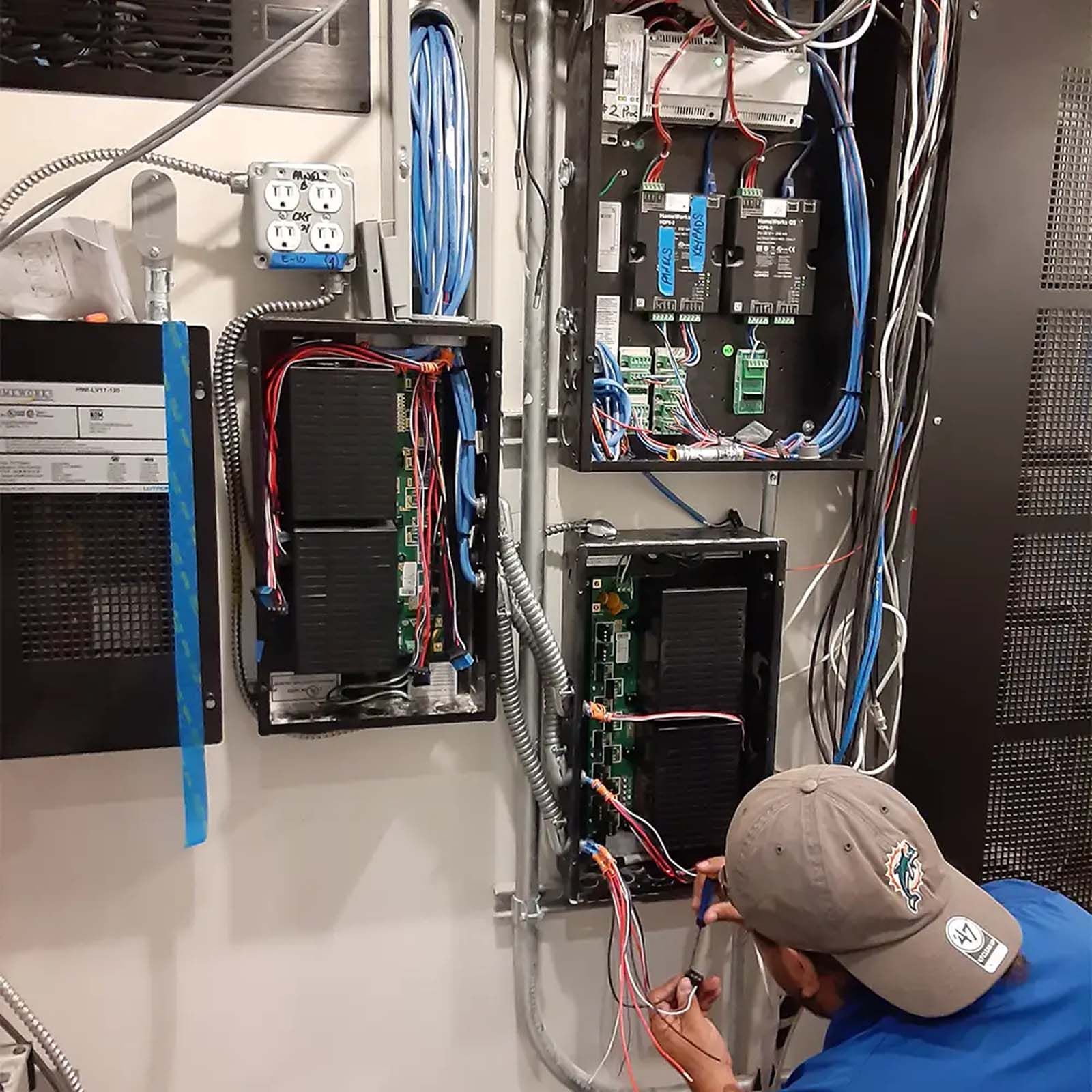 A man in a baseball cap is working on a electrical box.