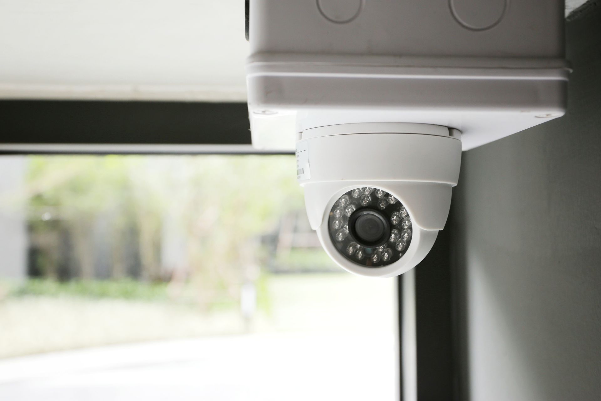 A security camera is hanging from the ceiling next to a window.