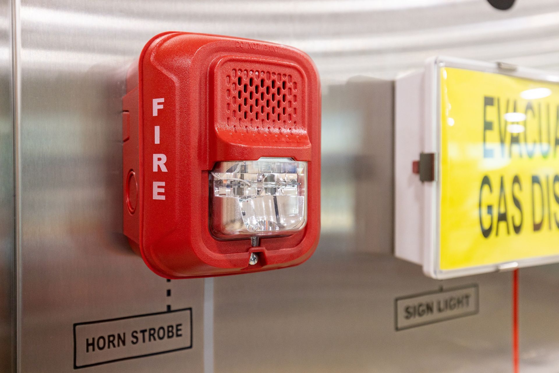 A red fire alarm is sitting on a stainless steel wall next to a yellow evacuation sign.