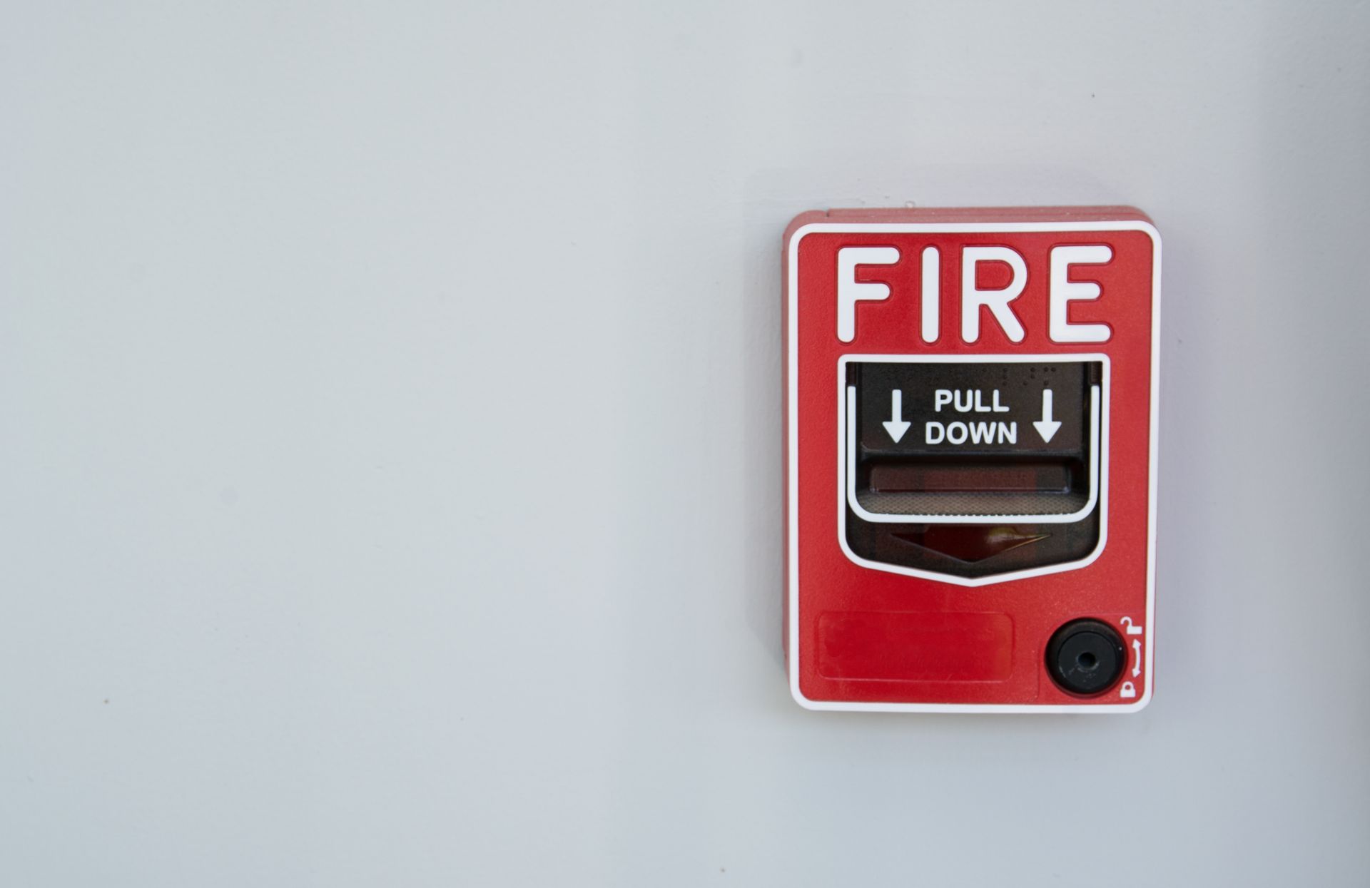 A red fire alarm is hanging on a white wall.