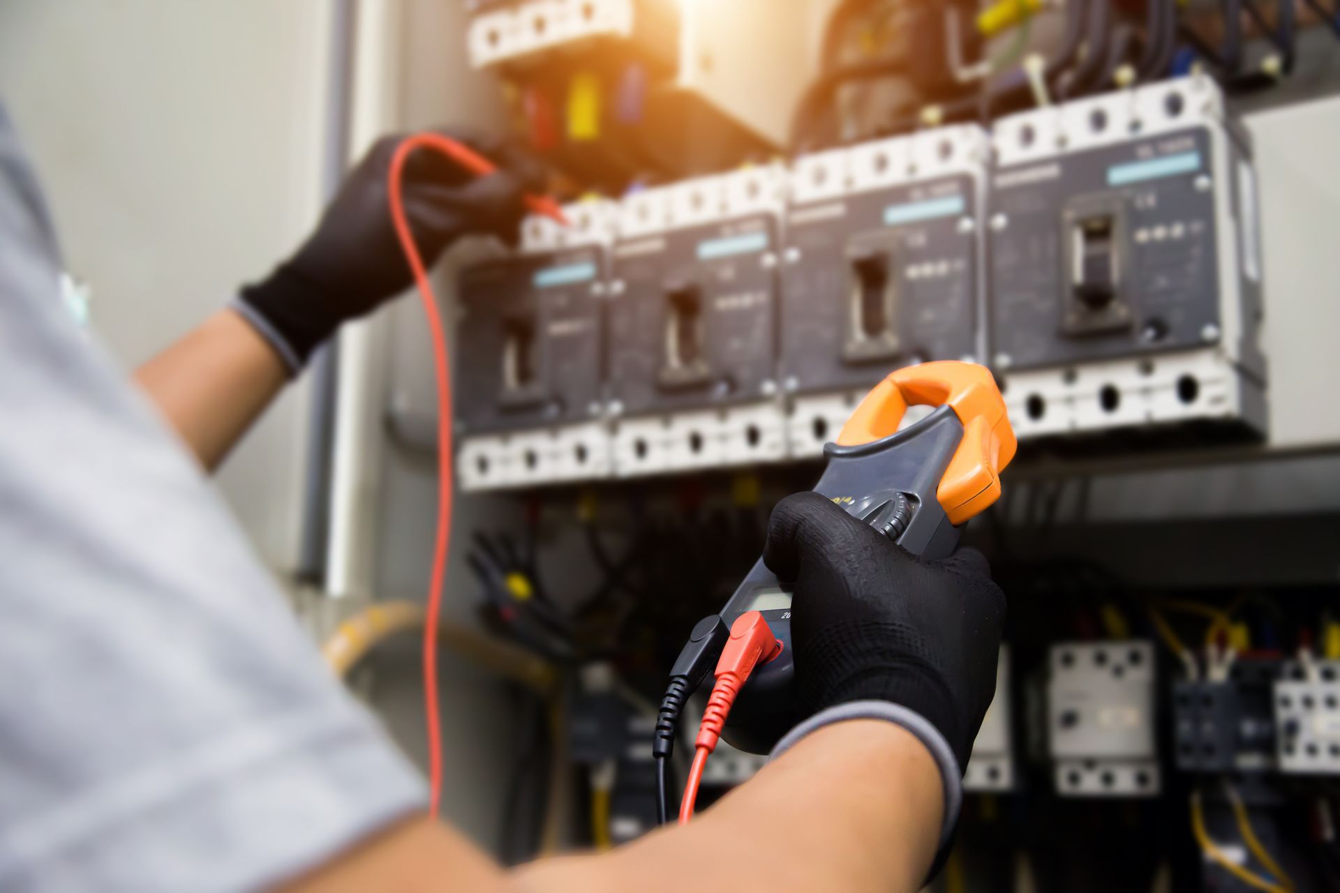 An electrician is working on an electrical panel with a clamp.