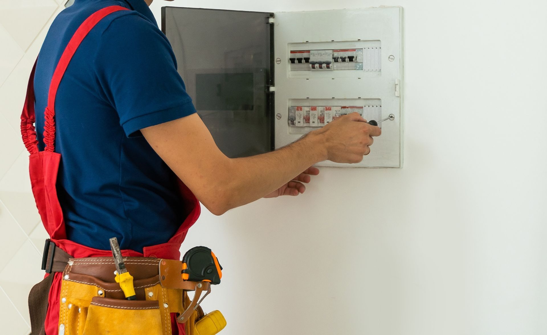 A man is working on an electrical box on a wall.