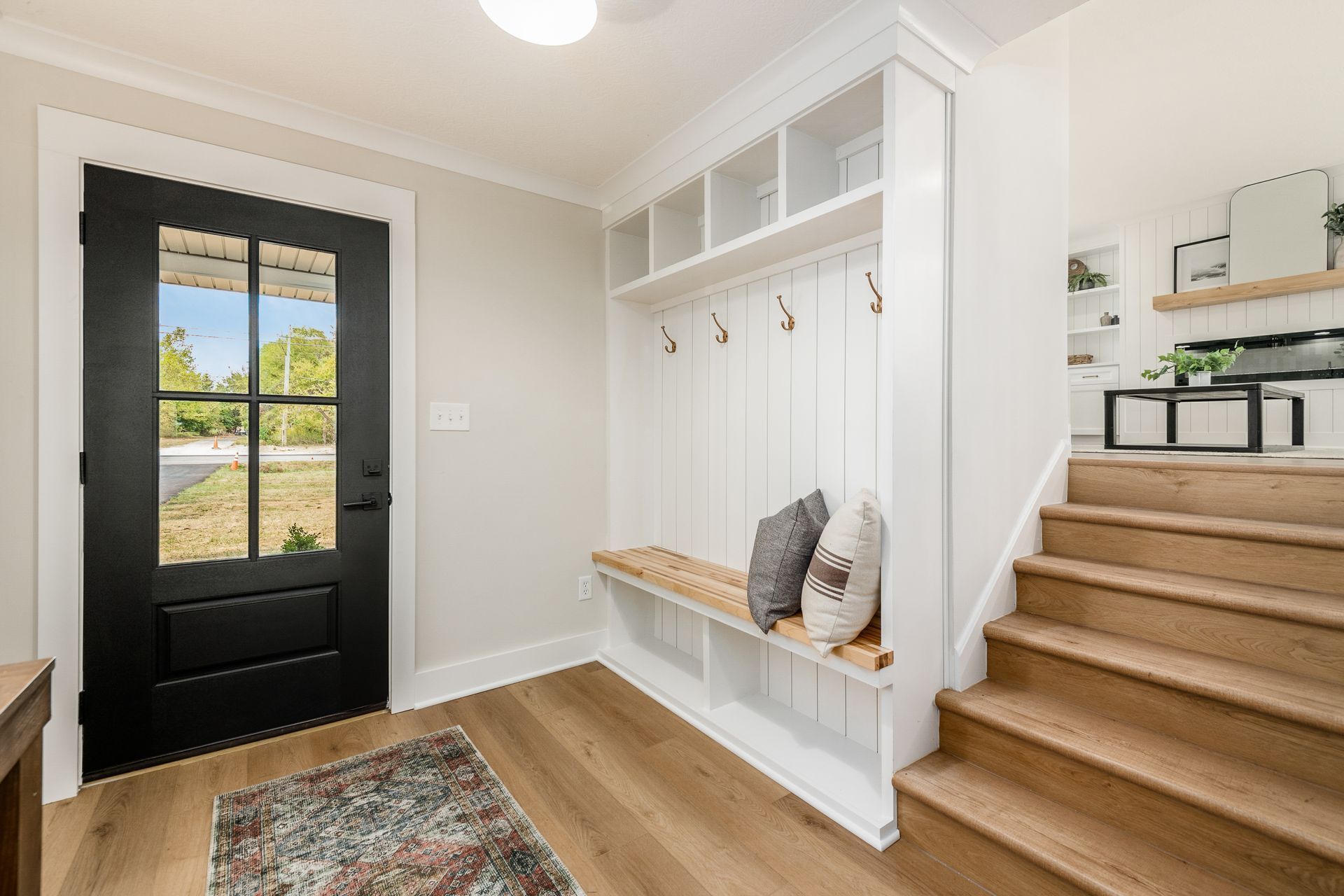 A hallway with a black door , a bench , and stairs.