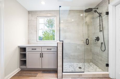Modern bathroom with glass shower, gray tile, wooden floor, and light gray cabinetry.