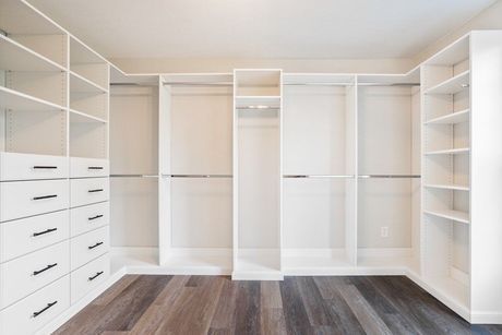 Empty white walk-in closet with shelves, drawers, and hanging rods. Dark wood floor.