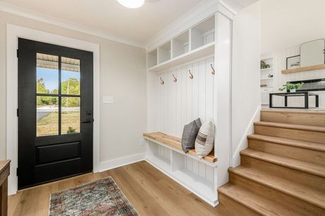A modern entryway with black door, white mudroom, wood bench, and staircase.