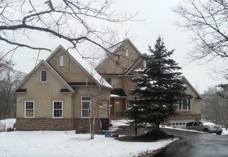 Two-story house in winter, beige siding with brick, snow on the ground, evergreen tree, and a truck in the driveway.