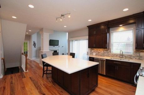 Modern kitchen with wooden floors, dark cabinets, white countertop island, and stainless steel appliances.
