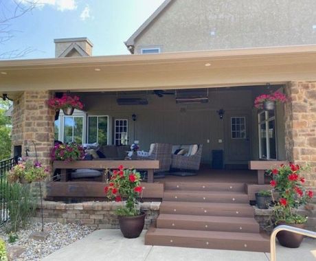 Covered patio with stone and brown features, furnished with seating and flowering plants.