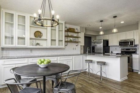 Modern white kitchen with island, metal chairs, round table, and open shelves.