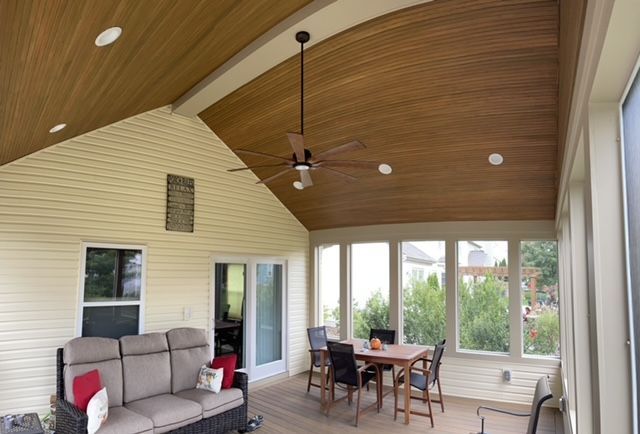 A screened in porch with a table and chairs and a ceiling fan.