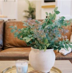 White vase with greenery and lavender sprigs on a brass tray, candle nearby, in front of a leather couch.