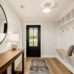 Entryway with black front door, built-in bench and shelves, wooden table, and a round mirror.