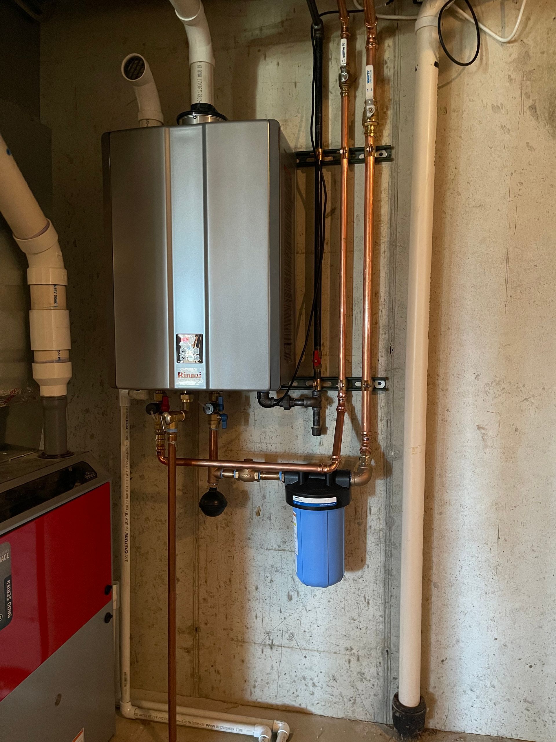 A person in overalls and a cap adjusting a white water heater's control panel