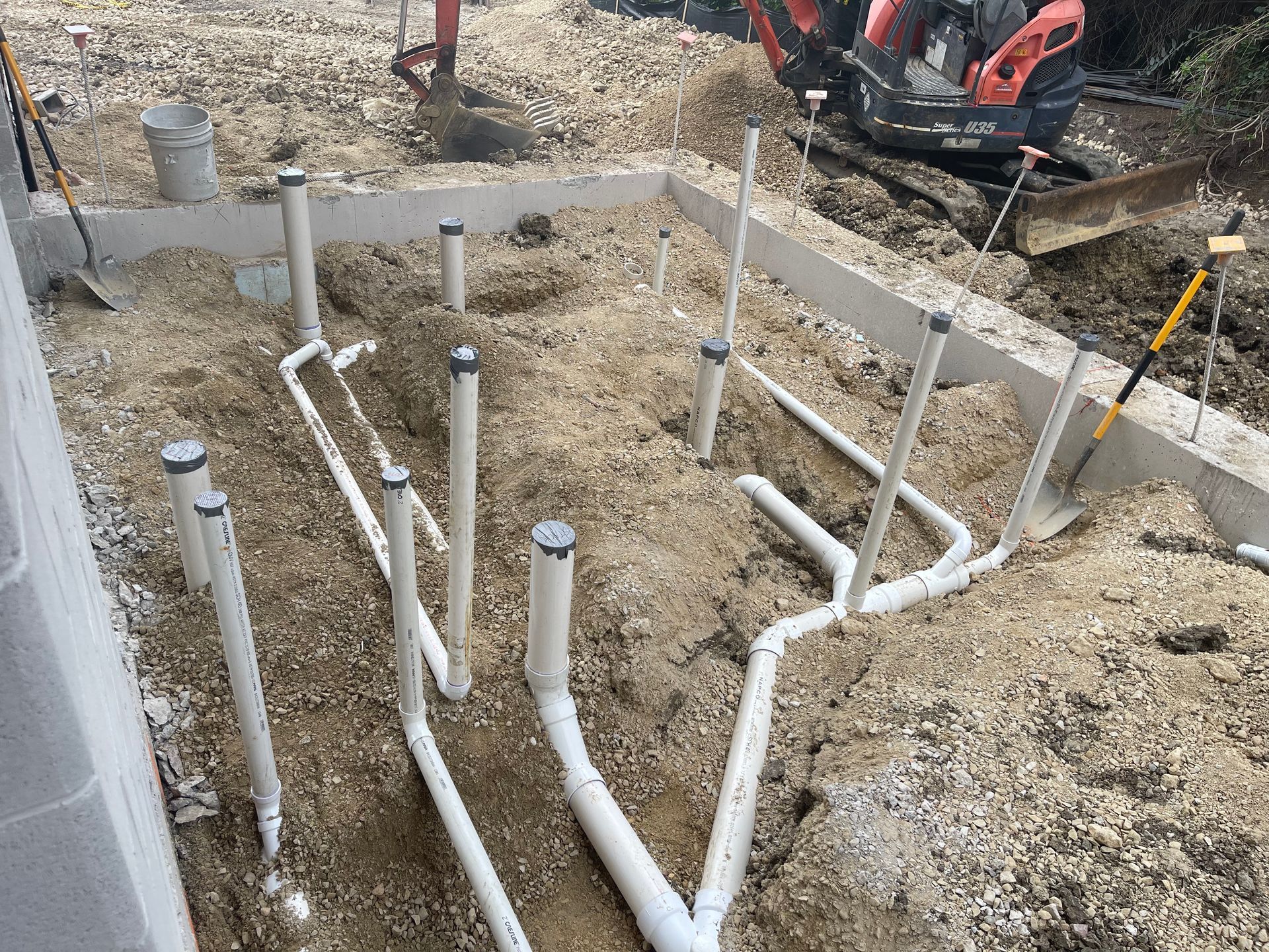Piping for plumbing system laid in trench in a construction site, near concrete foundation.