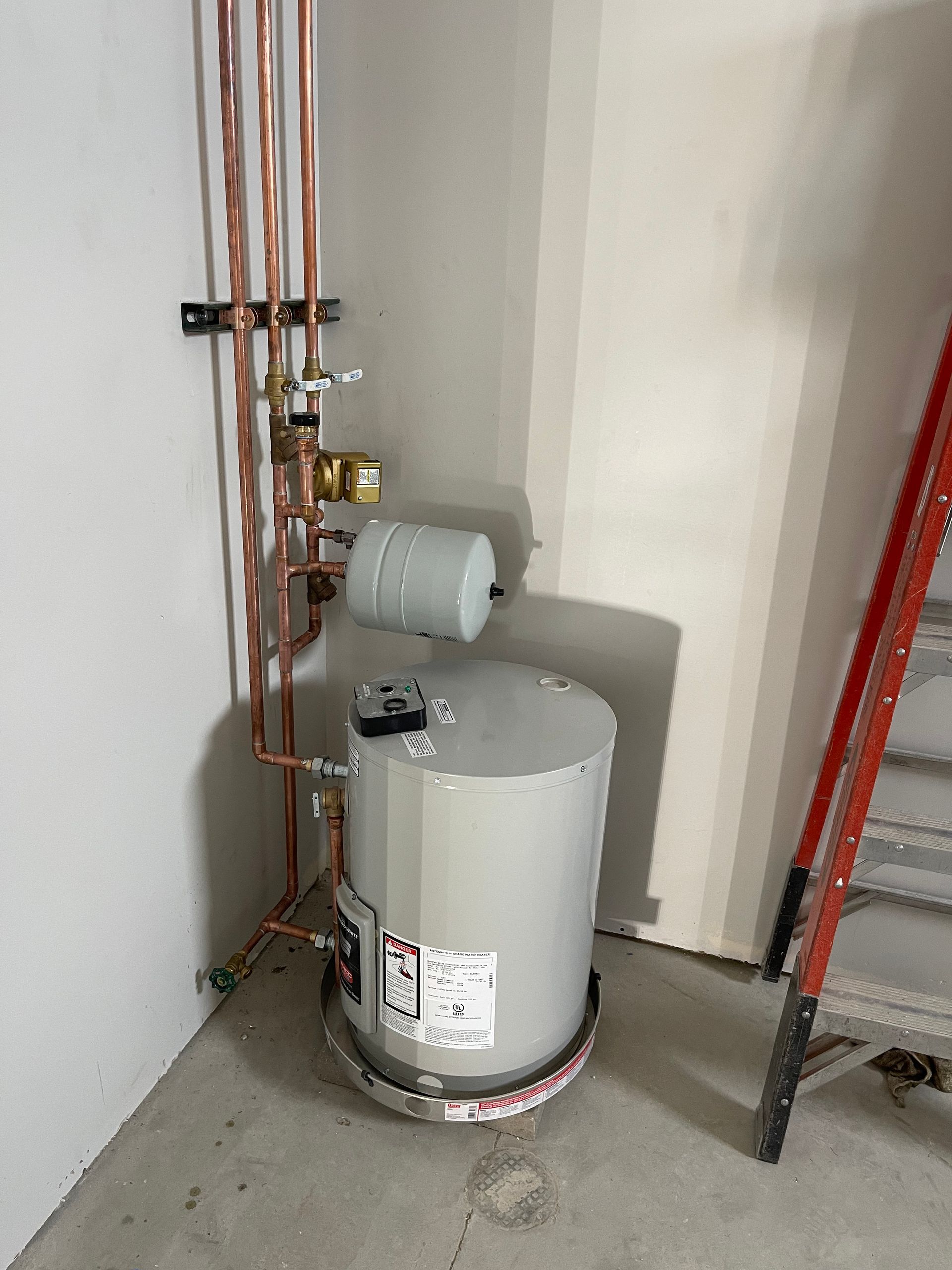 Water heater with copper pipes in a corner, next to a ladder.