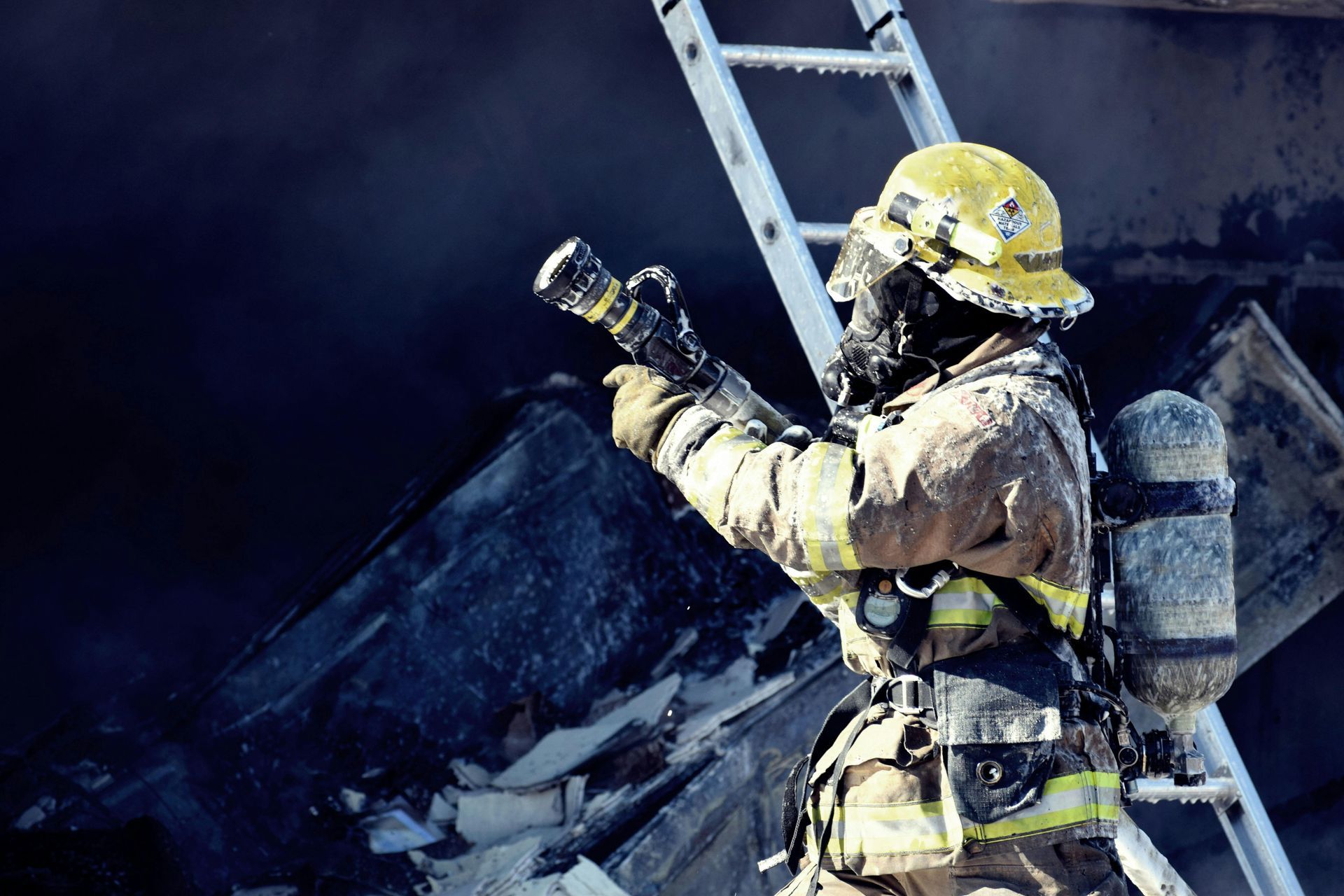 A fireman is standing on a ladder holding a hose.