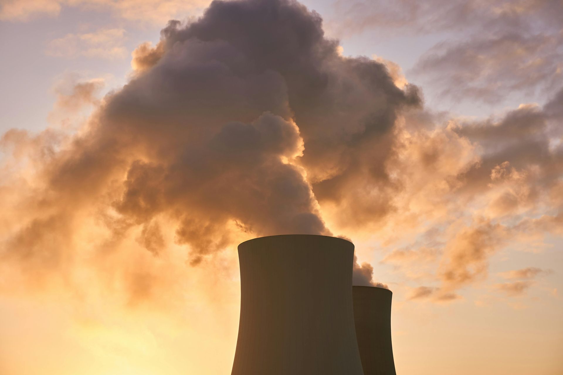 A nuclear power plant with smoke coming out of the cooling towers at sunset.