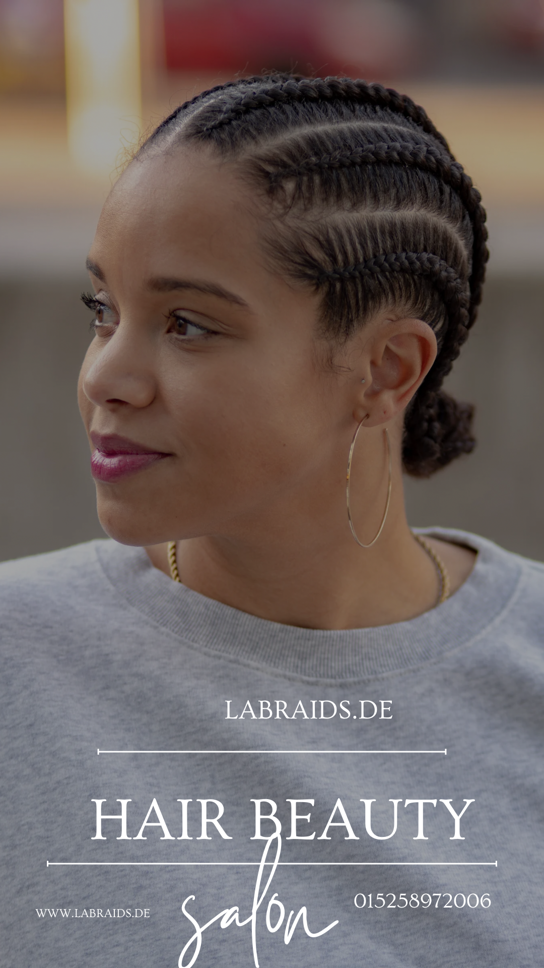 Eine Frau mit Zöpfen im Haar trägt ein graues Hemd und Ohrringe.