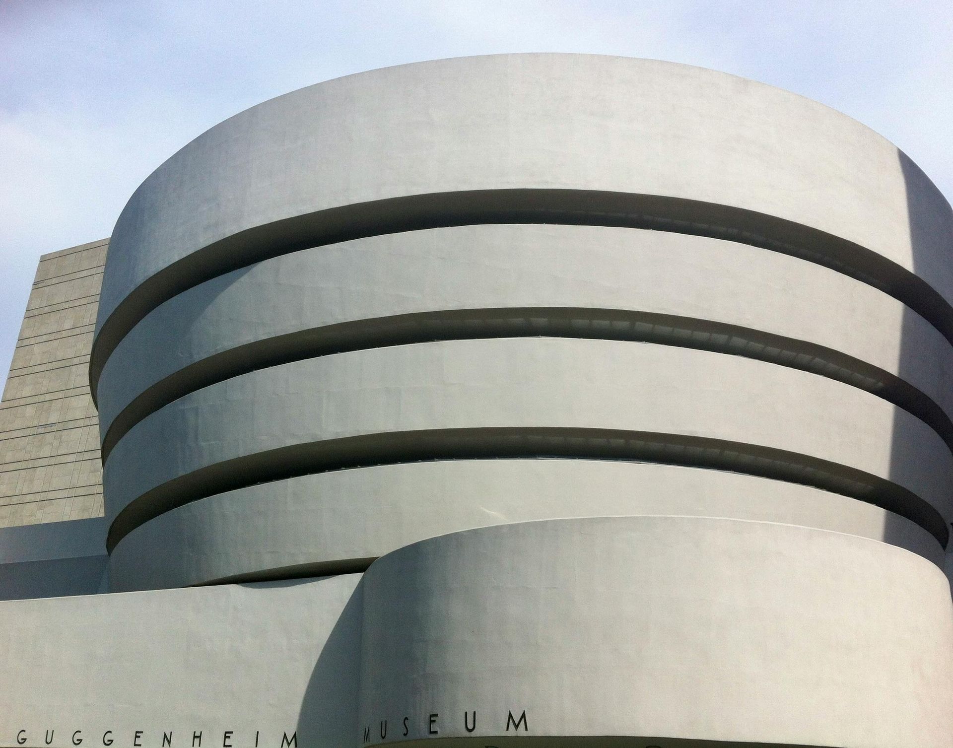 Solomon R. Guggenheim Museum, New York City: White cylindrical building with dark horizontal bands, against a blue sky.