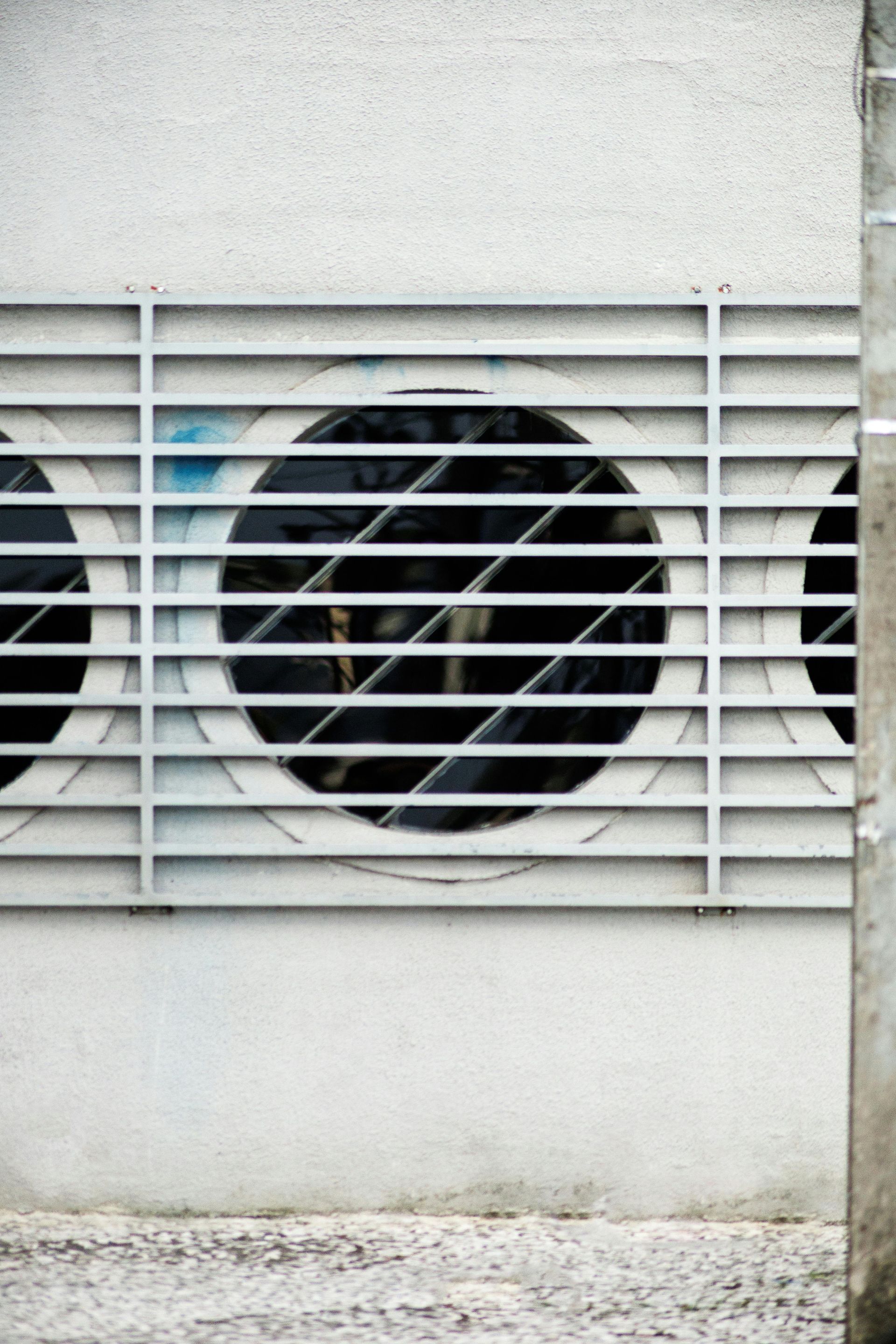 Circular ventilation openings with metal grates on a white wall.