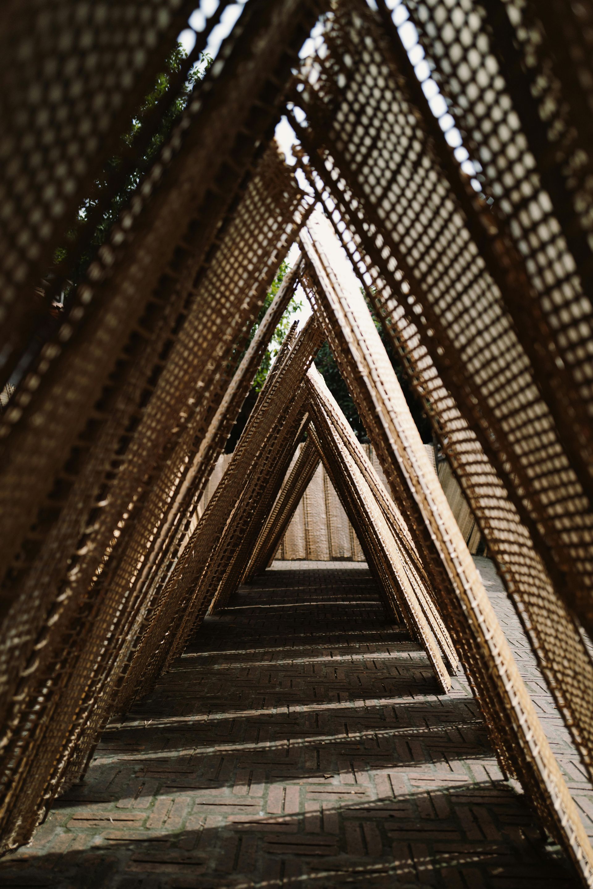 Triangular bamboo structure creating a pathway; natural light and shadows; textured ground.
