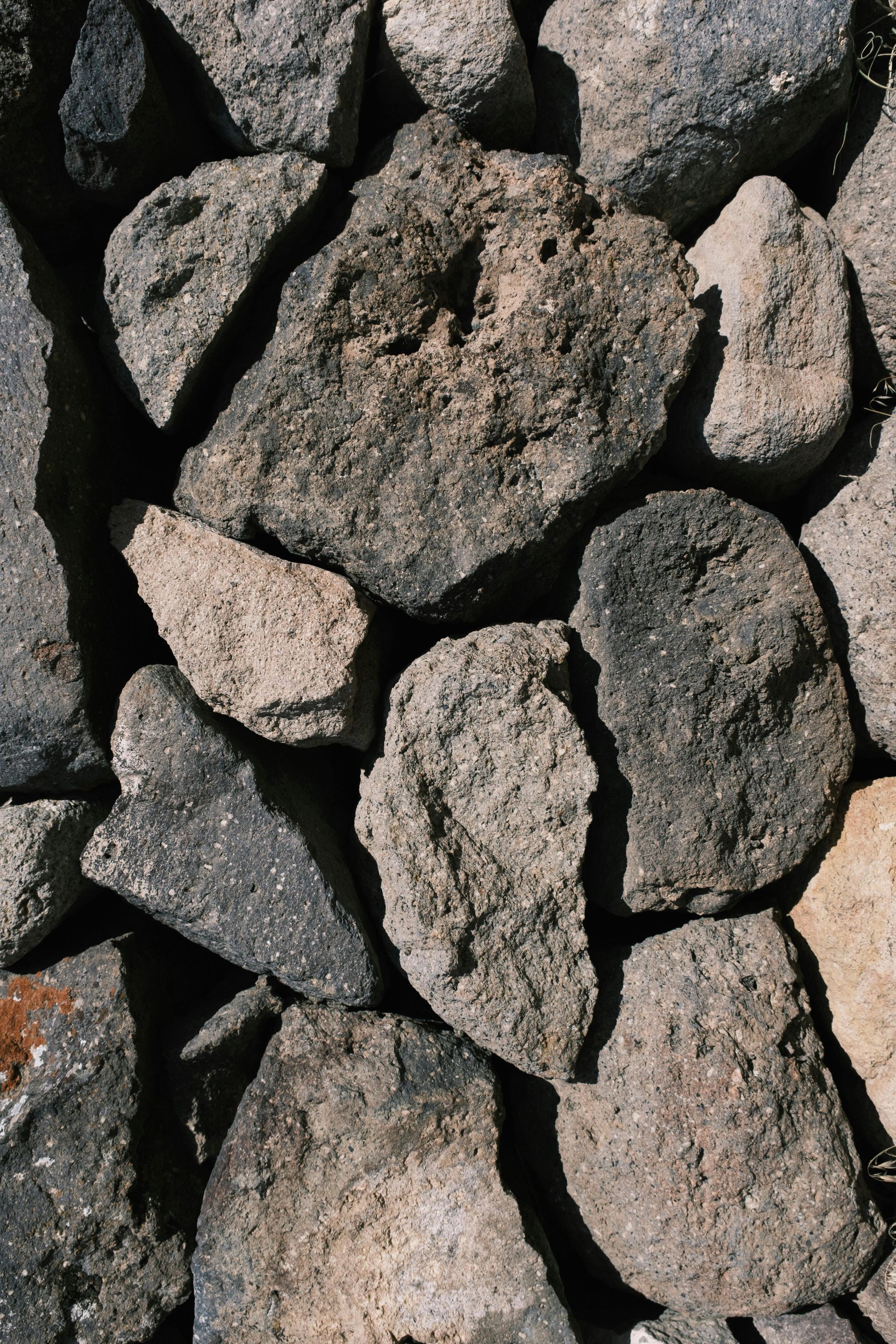 Rough, gray stone wall. Close-up view of irregularly shaped rocks tightly fitted together.