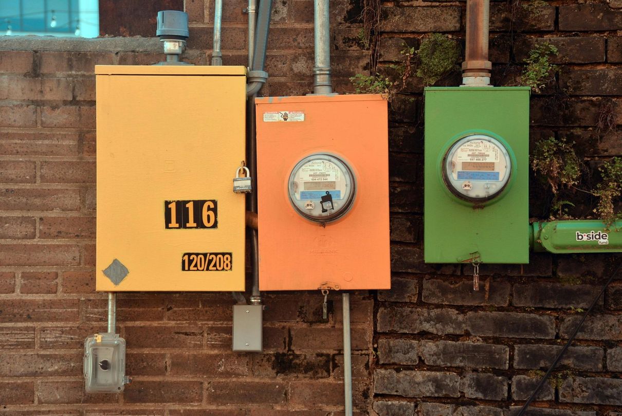 Yellow, orange, and green electrical boxes on a brick wall, numbered and with meters.