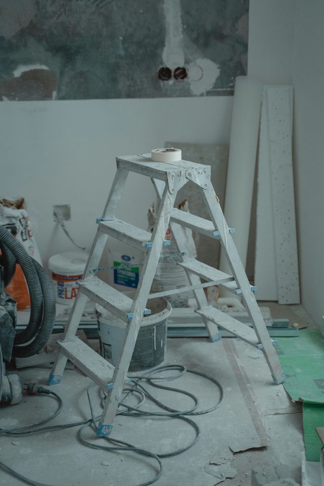 Aluminum step ladder inside a room under construction with paint and tools.